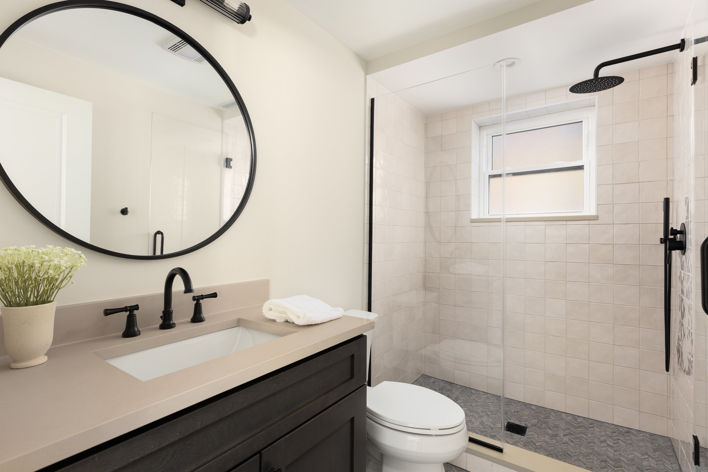 Bathroom with dark wood cabinetry, quartz countertop, and tiled shower